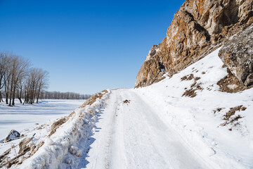 The road is covered with snow over the horizon against the background of a blue sky. Winter road in the mountains. Clear weather.