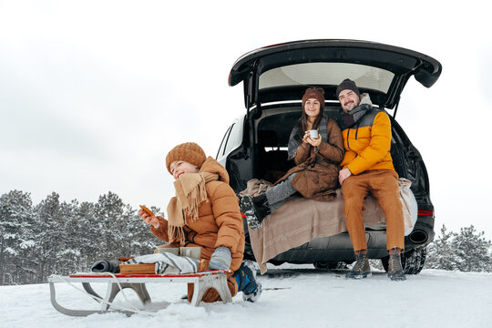 Winter Portrait Of A Family Sit On Car Trunk Enjoy Their Vacation In Forest