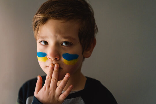 Portrait of a Ukrainian boy with a face painted with the colors of the Ukrainian flag. Ukrainian boy asks to stop the war in Ukraine. War of Russia against Ukraine.