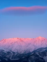 Foto op Plexiglas Lavendel Morgenroth schittert roze in de noordelijke Alpen in de winter, verlicht door de zonsopgangzon op het bergoppervlak. De wolken die in de lucht zweven zijn ook roze.