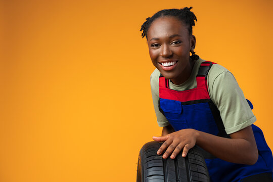 Portrait Of Smiling Black Female Mechanic Posing With New Car Tyres In Studio