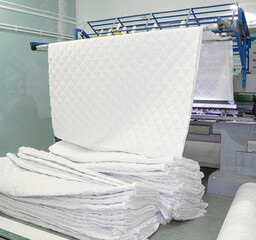 huge sewing machine in the workshop produces a sheet of quilt, mattress pad, pillow covers, bedspreads. Multi-needle machine embroiders a pattern with threads on a white cotton fabric and winterizer