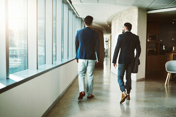 Fototapeta premium Success doesnt happen until people get moving. Rearview shot of two young businessmen walking down a corridor of a modern office.