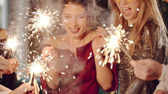 Asian girl and group young college student friends lit light sparkler in hand fireworks, sing and dance together. Woman on Party with people, love friendship relationship and celebration concept.