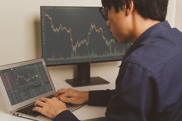 Young Asian Trader, investor or businessman is using on laptop, smartphone on trading stock market graph, candlestick chart as Bitcoin Cryptocurrency price chart. Investing money trader concept. - 493034445