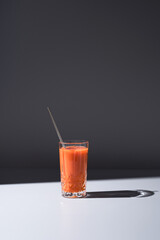 Vaso de jugo de zanahoria servido con una paja sobre fondo gris	
