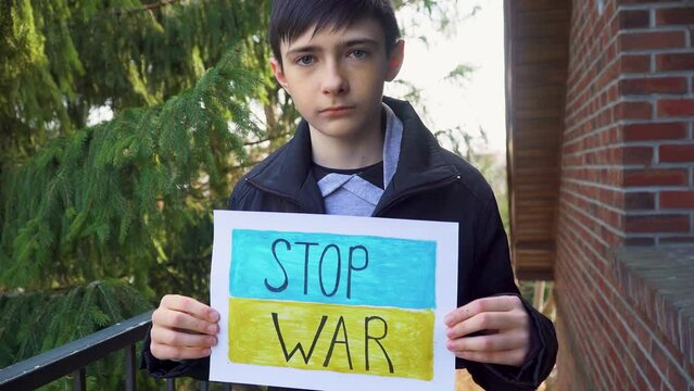 Ukrainian poor boy kid homeless protesting armored conflict holding banner with inscription message text Stop War on background of yellow blue flag. Crisis, peace, stop aggression in whole world