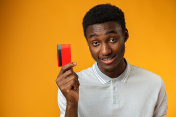 Afro american man holding red credit card against yellow background in studio