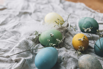 Easter eggs on rustic linen napkin with tender flowers. Stylish natural dyed pastel colorful egg, spring flowers and feathers composition. Happy Easter! Rustic still life
