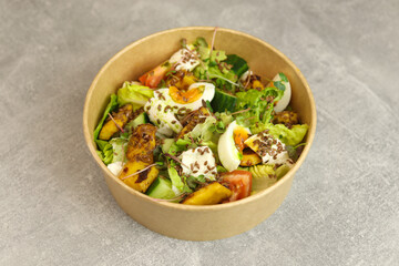 Healthy bowl with fried squid, egg, tomatoes, cucumbers, lettuce, cream cheese and flax seeds salad isolated on gray background. Food delivery service and daily ration concept.