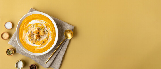 Wide banner pumpkin puree soup with cream, toast and seeds on a colored background with copy space....