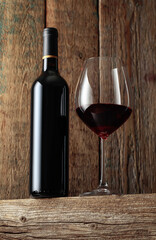 Bottle and glass of red wine on an old wooden table.
