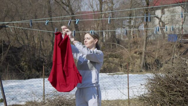 A young woman housewife hangs up the laundry in the backyard of the house.