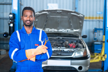 portrait shot of fsmiling Car mechanic wih tool in hand looking at camera while standing with arms...