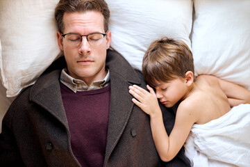 Sad caucasian father lying with little son before leaving for long business trip, upset dad came to say goodbye to sleepy child at home. family separation, good bye, farewell concept. top view