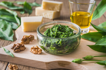 Homemade wild garlic pesto in a glass bowl on wooden background, decorated with some of the ingredients