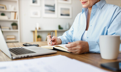 Crop middle aged businesswoman taking notes in notepad