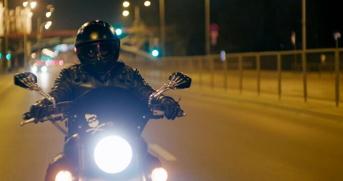 Biker is Riding Motorcycle on City roads and streets at late night. Motorcyclist drives Motorbike in evening with lights. Close up to wheel with copy space on asphalt. 4K medium tracking shot