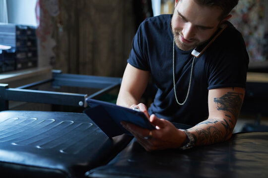 Caucasian Tattoo Artist Talking By Mobile Phone And In Tattoo Studio