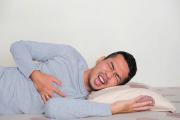 Adult Asian man suffering from chest pain when sleeping in his bed