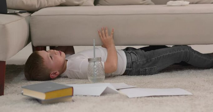 The child lies on the floor in front of her drawing sheets and a glass of water.