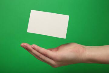 Hand with flying business card on green background.