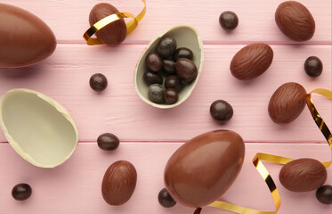 Easter composition with chocolate eggs and brown ribbon on pink wooden background.