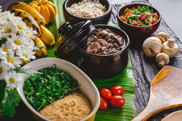 FEIJOADA VEGETARIANA DE COGUMELOS NA CUMBUCA PEQUENA COM ACOMPANHAMENTOS ARROZ, COUVE, FAROFA, BANANA DECORADA COM FOLHA DE BANANEIRA E FLORES