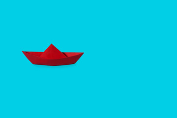 Red paper boat on a blue background. Overcoming difficulties and leadership concept. Free space for...