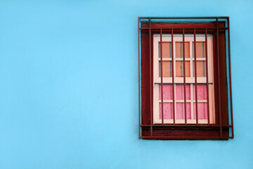 Blue wall and red small barred window. An old blue painted building with a solitary window and bars. Free space for text and ads