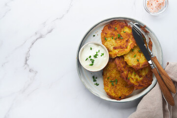 Potato pancakes. Fried homemade potato pancakes or latkes with cream and green onions in rustic plate on white marble table background. Rustic style. Healthy food. Top view.