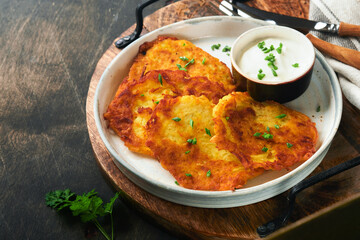 Potato pancakes. Fried homemade potato pancakes or latkes with cream and green onions in rustic plate on old wooden black table background. Rustic style. Healthy food. Top view.