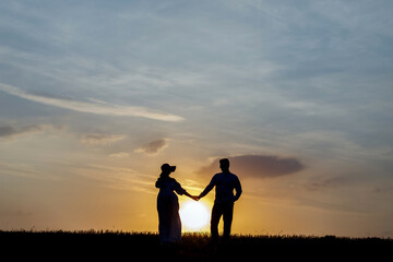 Young couple holding hands on the background of the setting sun on the horizon