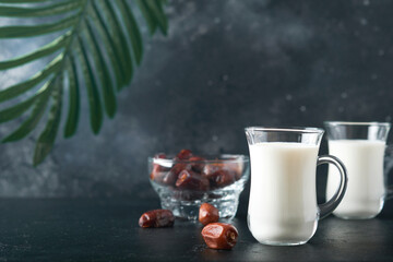 Ramadan Kareem food and drinks. Plate of dates, glass of milk and date palm branch on black...