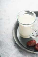 Ramadan Kareem food and drinks. Plate of dates, glass of milk and date palm branch on light grey background. Righteous Muslim Lifestyle. Place for text. Selective focus.