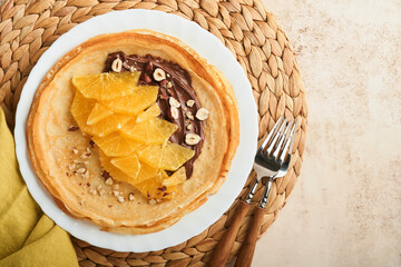 Crepes suzette with oranges. Thin crepes with chocolate spread, hazelnuts and orange slices fruit in white plate for breakfast on old concrete rustic table background. Copy space . Top view.
