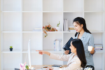 Consultation, discussion, marketing and investment concept, female employee holding folder and colleague pointing at a computer monitor to draw conclusions and assess investment risks for the company.