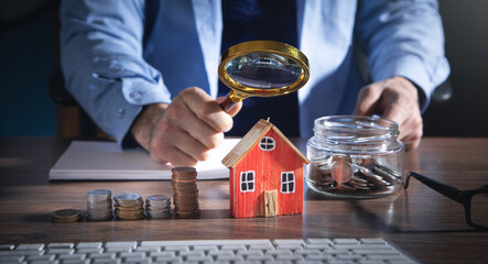 Real estate agent holding magnifying glass on house model.