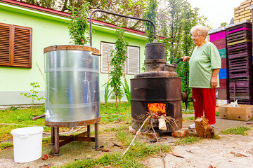 Obraz premium Woman is manually mixing fruit marc in distillation apparatus for making domestic alcohol liquor