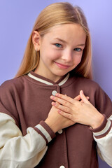 Little sincere adorable caucasian girl holding hands on chest feeling gratitude pose isolated on purple background, arms on heart gesture of love appreciation gratitude, adoption concept