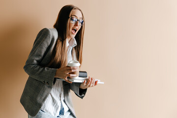 Clumsy intern, trying to hold everything with coffee cup, holding laptop and papers, opening her mouth, isolated on light brown background. First day at work concept