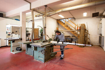 Studio portrait of a young carpenter while cutting a piece of wood with a circular saw