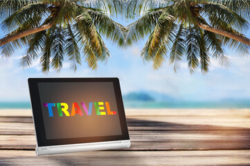 Colorful rainbow travel word on computer digital tablet on planks on tropical beach background....