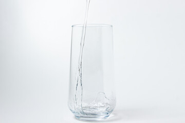 Drinking water is poured into a glass on a white background. Pure drinking water. Thirst quencher