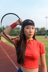 Asian young woman standing on the sport stadium and holding tennis racket