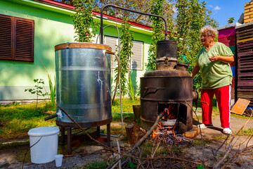 Woman is manually mixing fruit marc in distillation apparatus for making domestic alcohol liquor