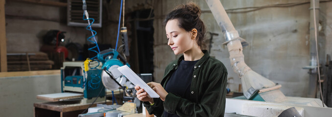 Young carpenter using digital tablet in workshop, banner.