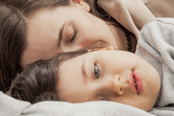 closeup loving mother with adorable little daughter relaxing in cozy bed enjoying lazy leisure time together, smiling caring mom hugging cute thoughtful preschooler