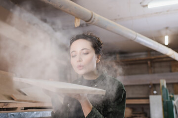 Fototapeta na wymiar Carpenter blowing sawdust from wooden plank in workshop.