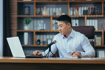 Focused smiling young businessman using professional microphone recording audio podcast, voice...
